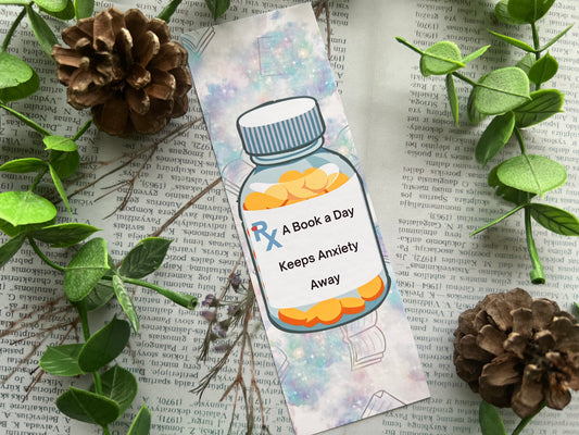 A bookmark with a pill bottle. On the pill bottle it reads a book a day keeps anxiety away.